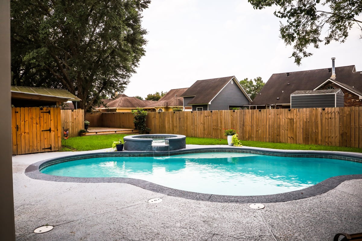 Large free form gray swimming pool with turquoise blue swim water in backyard
