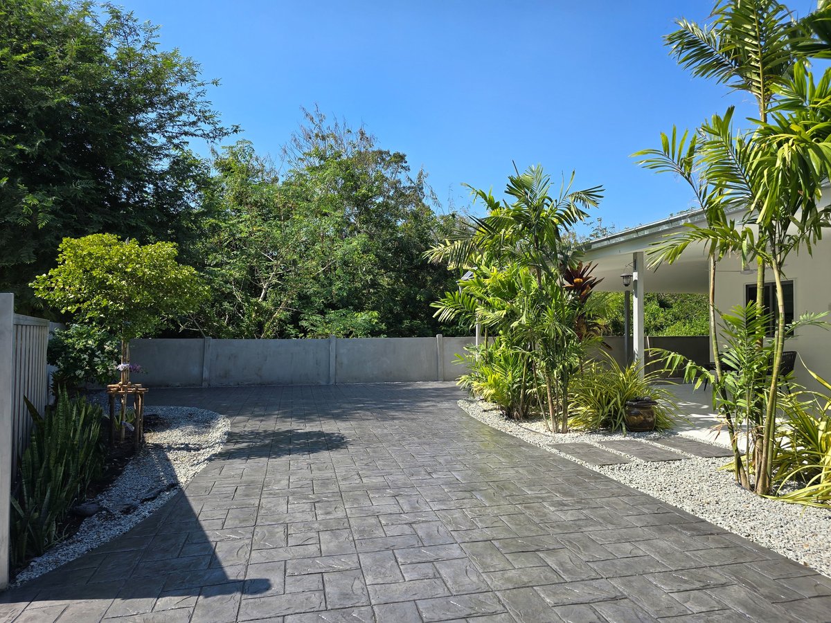 Stamped concrete driveway showcases intricate designs with lush plants framing this outdoor space