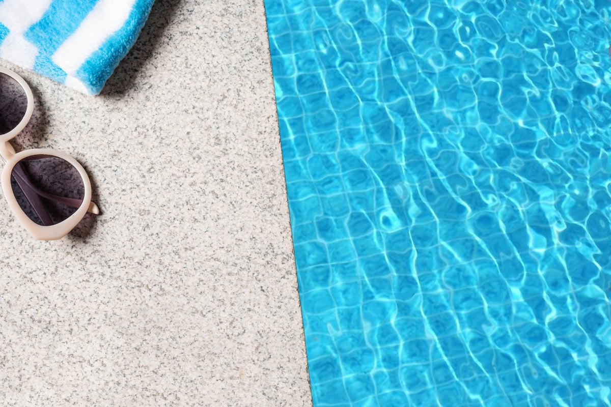Edge of pool with beach towel and sunglasses with blue pool water texture