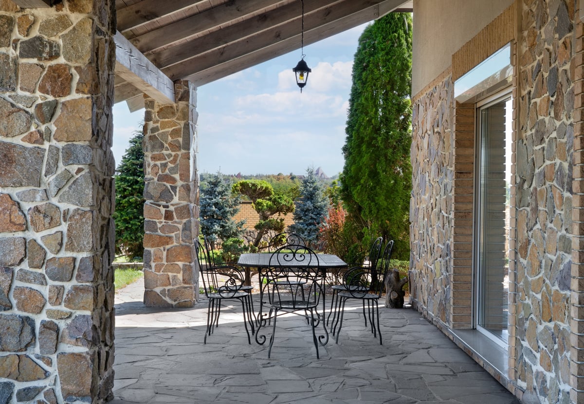 Covered stone terrace with wrought iron garden furniture in countryside house
