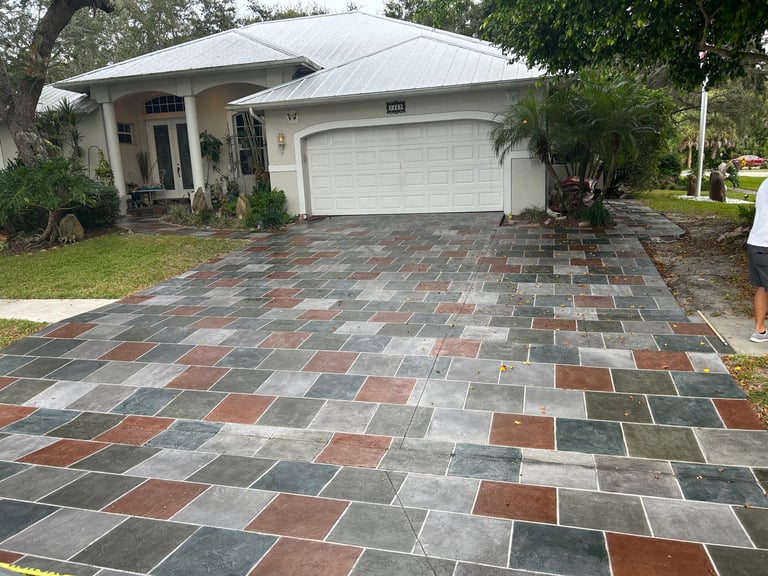 Modern single-story house with white garage door and metal roof on a colorful brick paver driveway lined with green vegetation