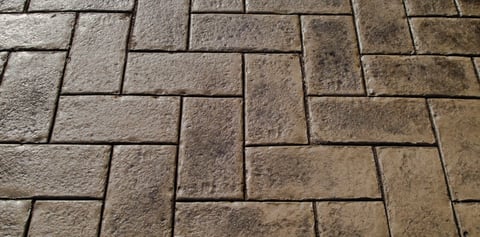 Close-up of tan and gray stone pavers arranged in a herringbone pattern